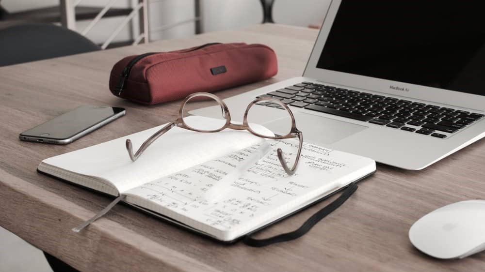 Mesa com notebook, celular e caderno para estudar o que fazer antes de pedir demissão.