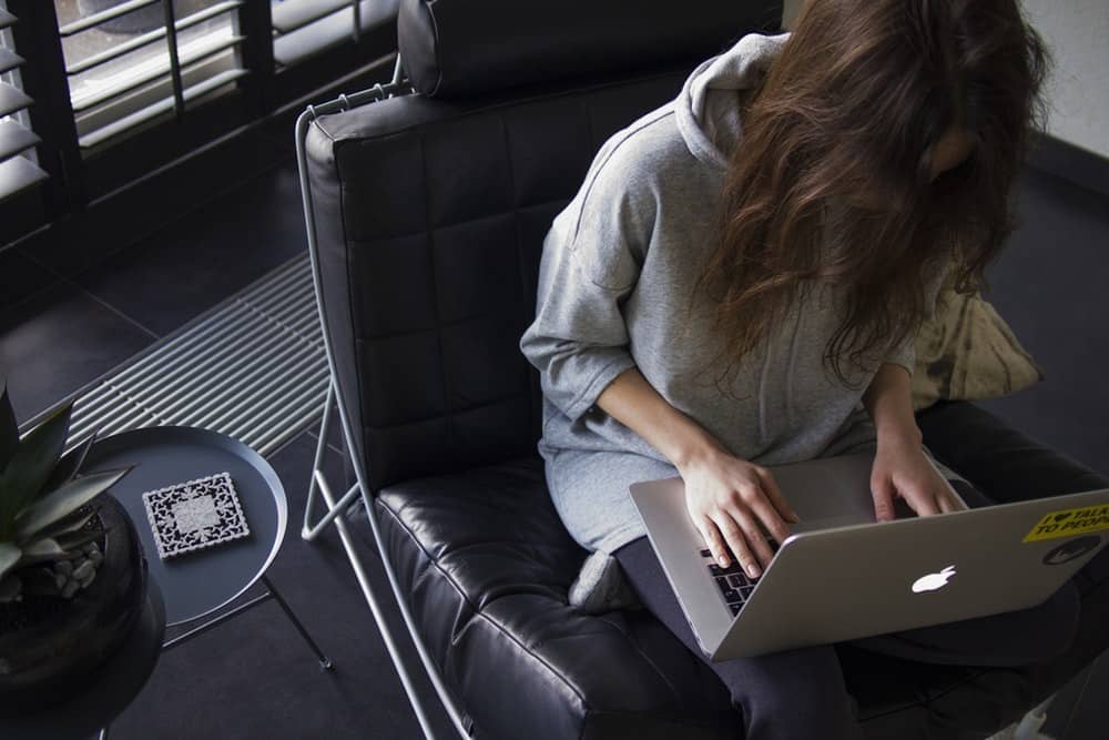 Pessoa sentada no sofá com notebook trabalhando em casa, home office